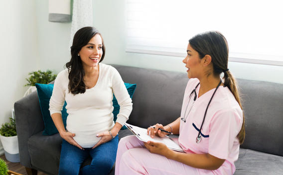 Nurse and expectant mother sitting on couch and talking